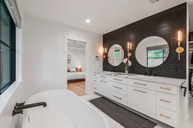 ensuite bathroom featuring a freestanding bath, double vanity, ensuite bath, and a sink