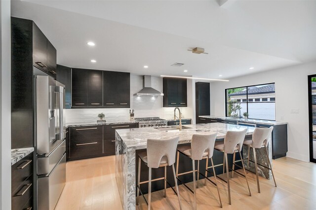 kitchen featuring high end refrigerator, modern cabinets, wall chimney exhaust hood, and a sink