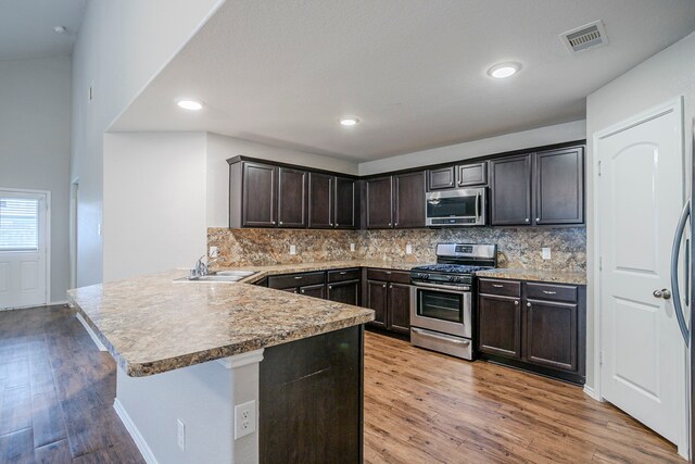 15459 Refugio Verde Way, Houston, TX 77049 - kitchen featuring a peninsula, dark brown cabinets, light wood-style flooring, a sink, and appliances with stainless steel finishes
