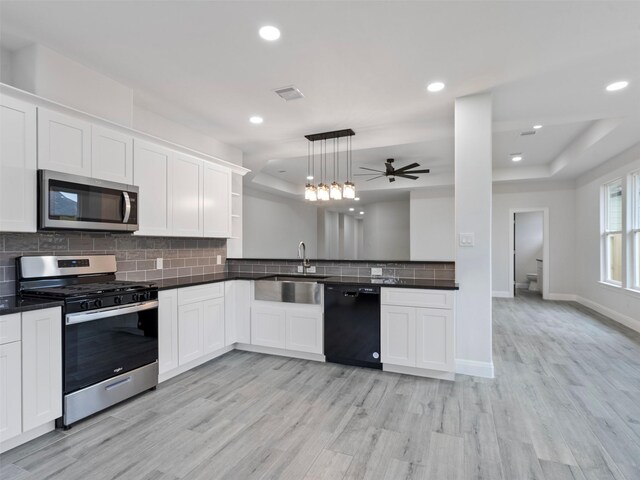 kitchen featuring dark countertops, ceiling fan, a raised ceiling, a sink, and stainless steel appliances