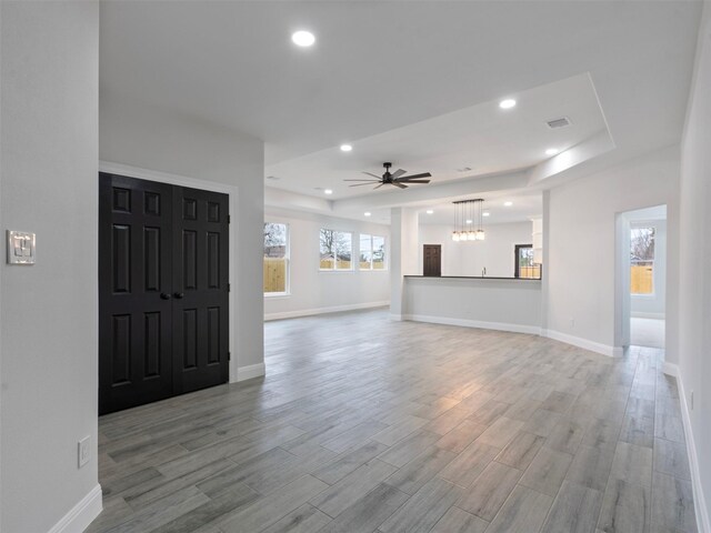 unfurnished living room featuring a raised ceiling, recessed lighting, baseboards, wood finished floors, and visible vents