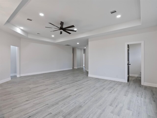 spare room featuring ceiling fan, visible vents, a raised ceiling, baseboards, and light wood-style floors