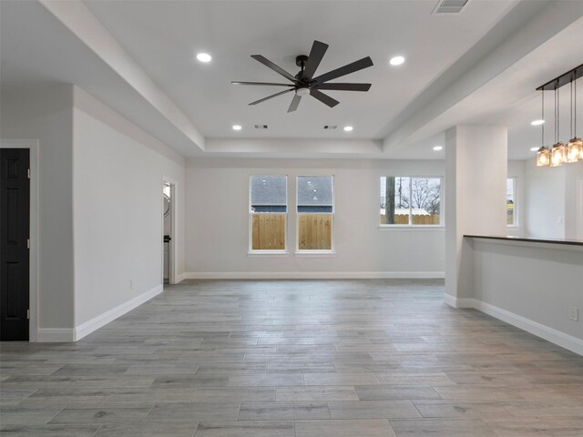 unfurnished living room featuring plenty of natural light, a ceiling fan, a tray ceiling, and wood finished floors