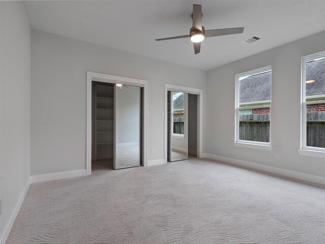 unfurnished bedroom with visible vents, multiple closets, baseboards, ceiling fan, and light colored carpet