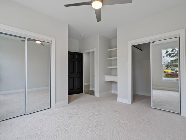 unfurnished bedroom featuring carpet floors, baseboards, ceiling fan, and two closets