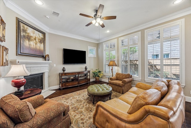 living room with crown molding, wood finished floors, baseboards, a fireplace with raised hearth, and a ceiling fan