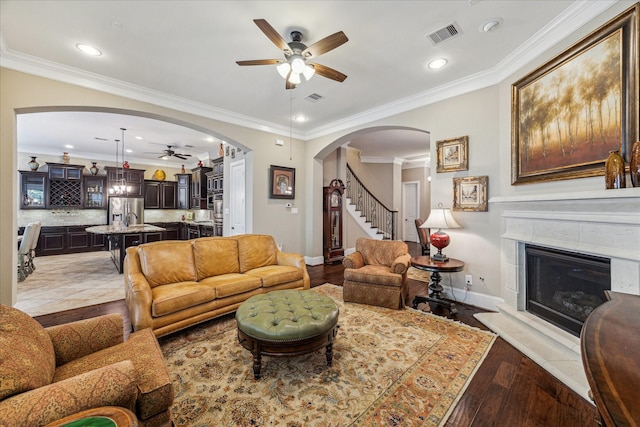 living area with visible vents, a glass covered fireplace, wood finished floors, ceiling fan, and arched walkways
