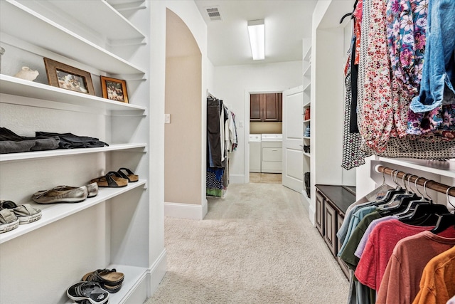 walk in closet with arched walkways, visible vents, independent washer and dryer, and light colored carpet