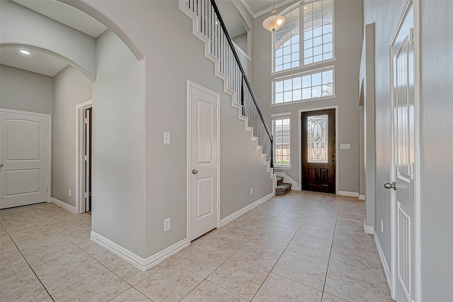 foyer featuring arched walkways, light tile patterned floors, baseboards, stairway, and a high ceiling