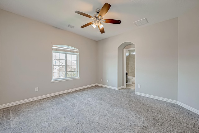 carpeted spare room with visible vents, arched walkways, baseboards, and ceiling fan
