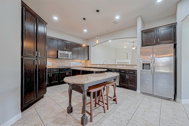kitchen with decorative backsplash, dark brown cabinets, arched walkways, appliances with stainless steel finishes, and light tile patterned floors