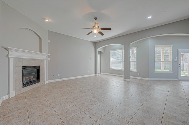 unfurnished living room featuring light tile patterned floors, a tiled fireplace, ceiling fan, and baseboards