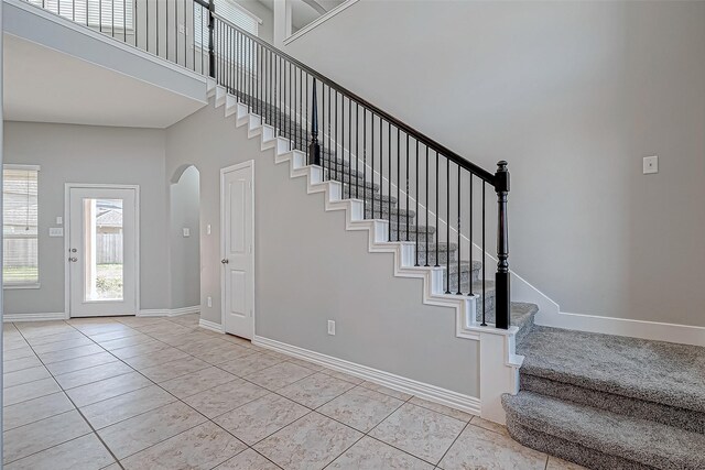 stairs with arched walkways, baseboards, tile patterned flooring, and a towering ceiling