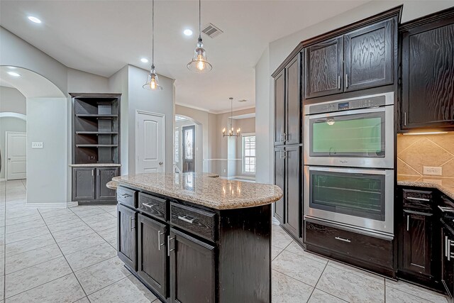 kitchen with double oven, arched walkways, backsplash, and light stone counters