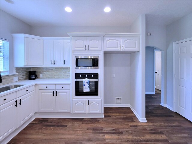 kitchen featuring arched walkways, a sink, stainless steel microwave, white cabinetry, and oven
