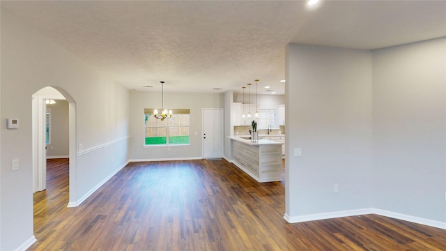 9267 Inlet Cir, Montgomery, TX 77356 - unfurnished living room featuring a chandelier, dark wood-type flooring, baseboards, arched walkways, and a textured ceiling