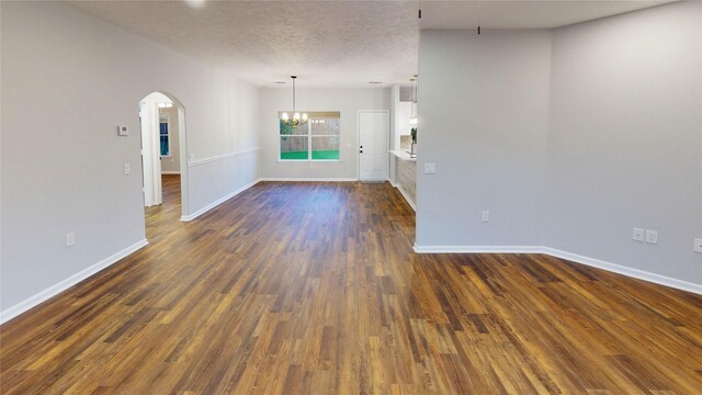 9267 Inlet Cir, Montgomery, TX 77356 - empty room with a chandelier, baseboards, dark wood-style floors, arched walkways, and a textured ceiling