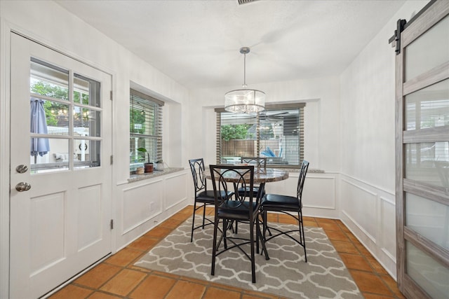 dining room featuring tile patterned flooring, wainscoting, a decorative wall, a barn door, and a notable chandelier