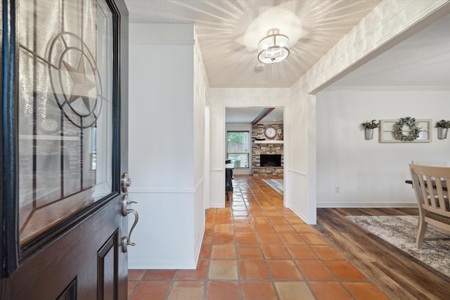 tiled entryway featuring baseboards, crown molding, a fireplace, and an inviting chandelier
