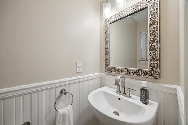 bathroom with a sink, a decorative wall, and wainscoting