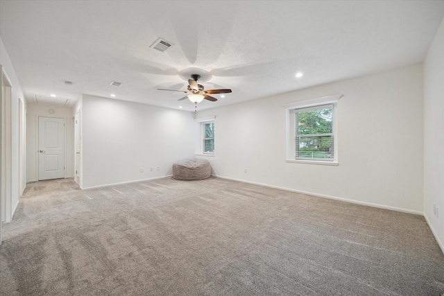 unfurnished room with a ceiling fan, light colored carpet, visible vents, and attic access