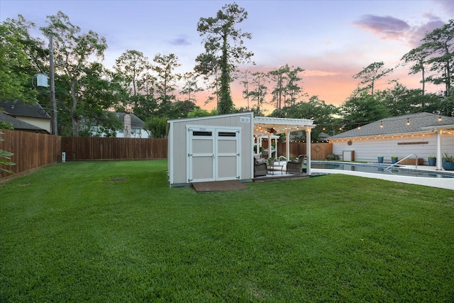 outdoor structure at dusk featuring a lawn, a fenced backyard, an outbuilding, and a storage shed