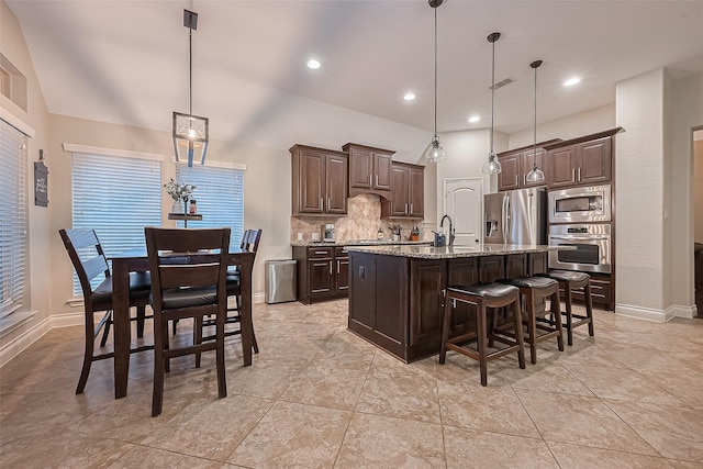 kitchen featuring dark brown cabinetry, appliances with stainless steel finishes, a breakfast bar area, an island with sink, and backsplash