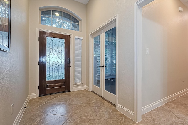 foyer featuring baseboards, a textured wall, and french doors