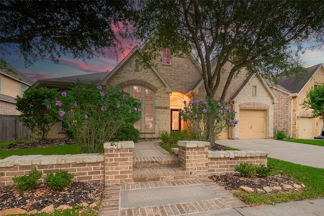 view of front of property featuring brick siding, fence, an attached garage, and driveway