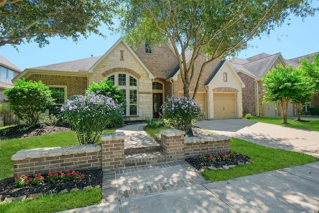 view of front of property with a garage, stone siding, roof with shingles, brick siding, and driveway