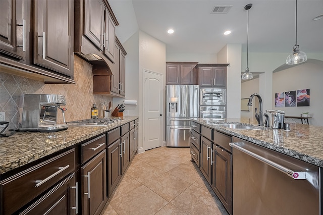 11918 Forest Moon Dr, Cypress, TX 77433 - kitchen with appliances with stainless steel finishes, a sink, dark brown cabinetry, dark stone countertops, and decorative backsplash