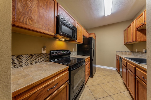kitchen with a sink, tile counters, light tile patterned floors, backsplash, and black appliances