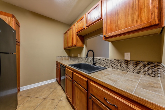 kitchen featuring tile countertops, brown cabinets, a sink, light tile patterned floors, and black appliances