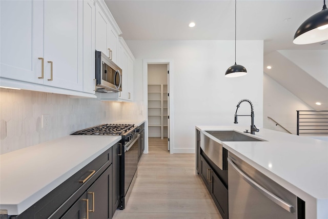 kitchen featuring white cabinets, a sink, light countertops, stainless steel appliances, and light wood-type flooring