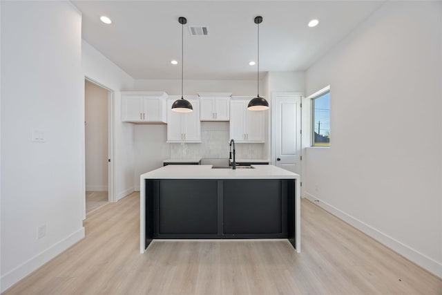 kitchen featuring a kitchen island with sink, light wood-style flooring, white cabinetry, tasteful backsplash, and visible vents