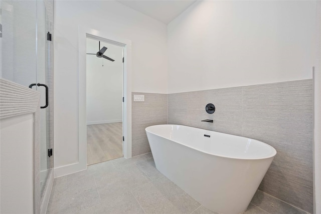 full bath with a ceiling fan, a freestanding tub, tile walls, a shower stall, and a wainscoted wall