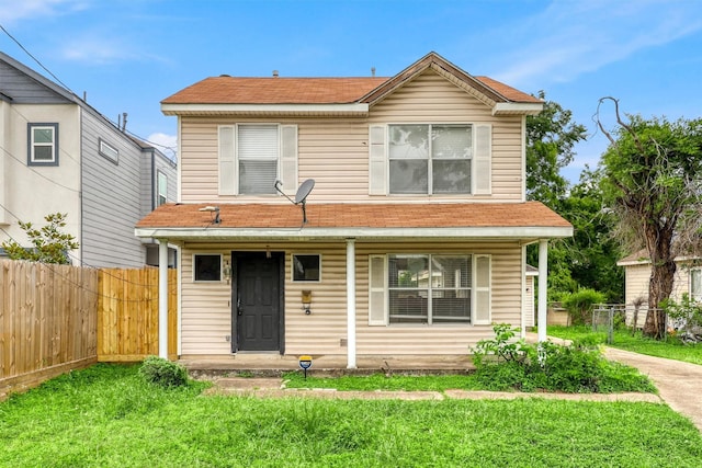 traditional-style home featuring covered porch, fence, roof with shingles, and a front lawn