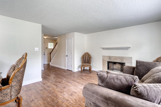 living area featuring a textured ceiling, baseboards, wood finished floors, a tile fireplace, and stairway