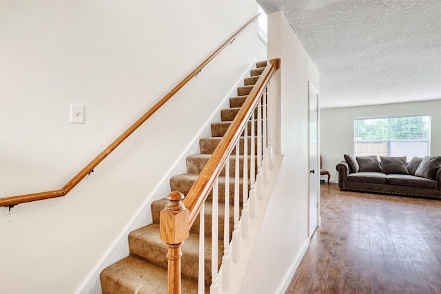 staircase with a textured ceiling, baseboards, and hardwood / wood-style flooring