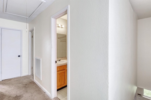 hall with a sink, attic access, light colored carpet, and visible vents