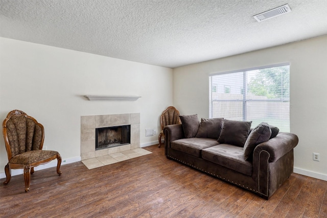 living room featuring visible vents, wood finished floors, a fireplace, baseboards, and a textured ceiling
