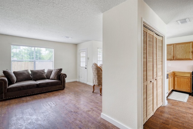 living room with visible vents, baseboards, a textured ceiling, and wood finished floors