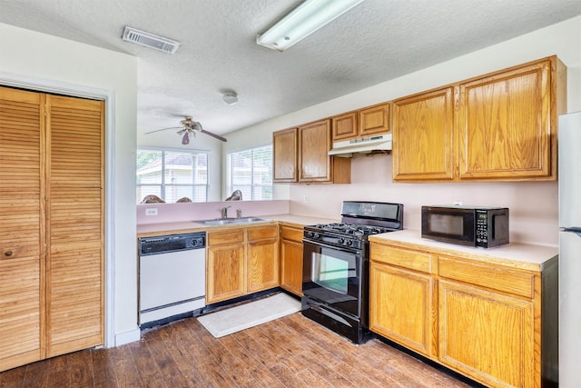 kitchen with a sink, light countertops, under cabinet range hood, visible vents, and black appliances