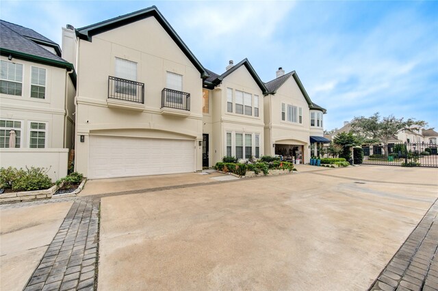 multi unit property with a garage, fence, a balcony, concrete driveway, and stucco siding