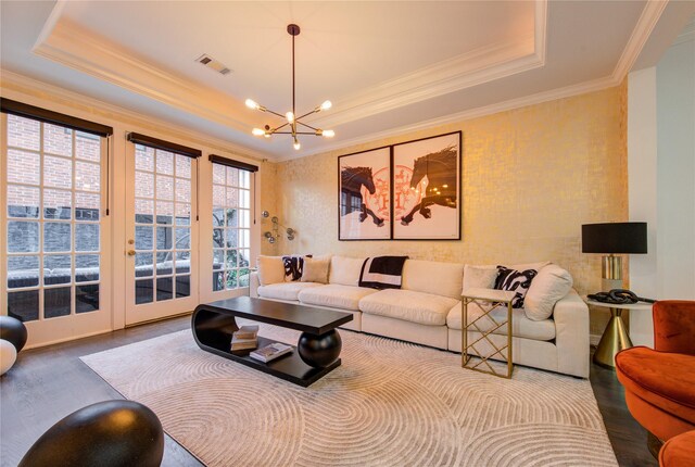 living room with visible vents, wood finished floors, a notable chandelier, ornamental molding, and a tray ceiling