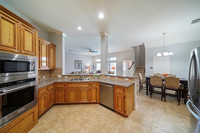 kitchen with brown cabinetry, a peninsula, ceiling fan with notable chandelier, a sink, and appliances with stainless steel finishes