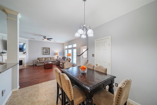 25702 Serene Spring Ln, Spring, TX 77373 - dining space with stairway, a ceiling fan, a fireplace with flush hearth, a chandelier, and light tile patterned floors