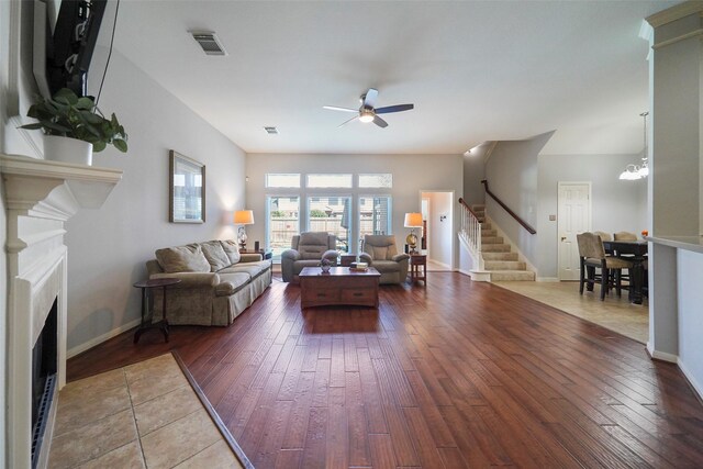 living room with visible vents, stairway, hardwood / wood-style flooring, a fireplace with flush hearth, and ceiling fan with notable chandelier