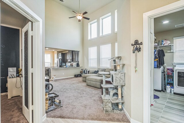 carpeted living room with visible vents, a high ceiling, a wealth of natural light, and washing machine and clothes dryer