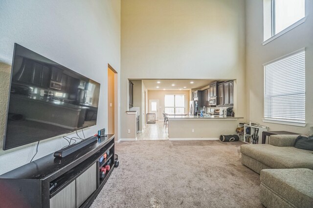 living area with baseboards, light colored carpet, and a towering ceiling